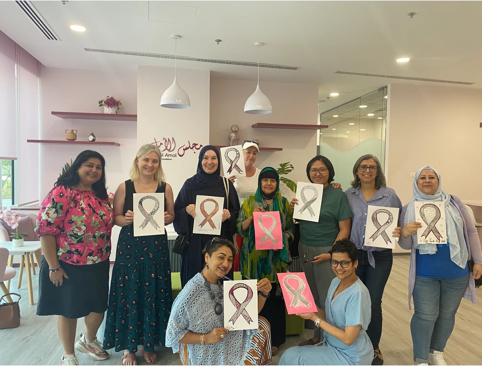 Cheshta Roy Sarkar with women holding ribbon-themed artworks at Majlis Al Amal